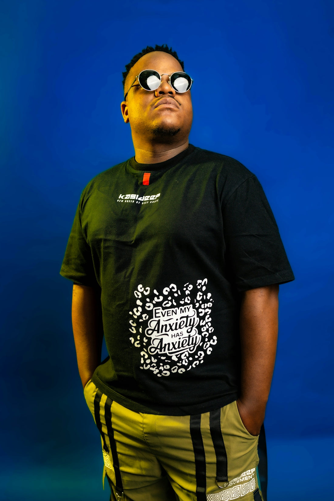 Man in sunglasses and graphic t-shirt stands against blue background.