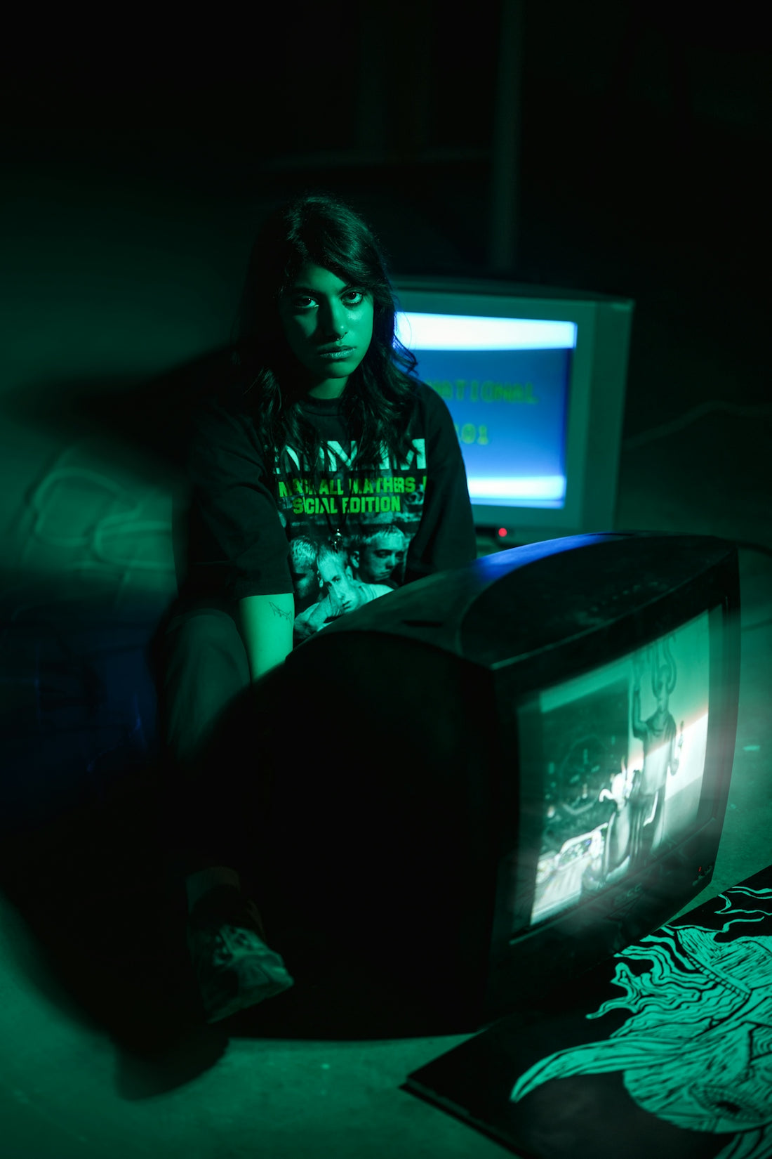 Woman sitting in green light with old televisions
