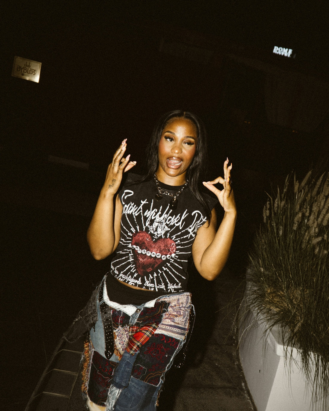 A woman poses with hands raised in a dark setting.