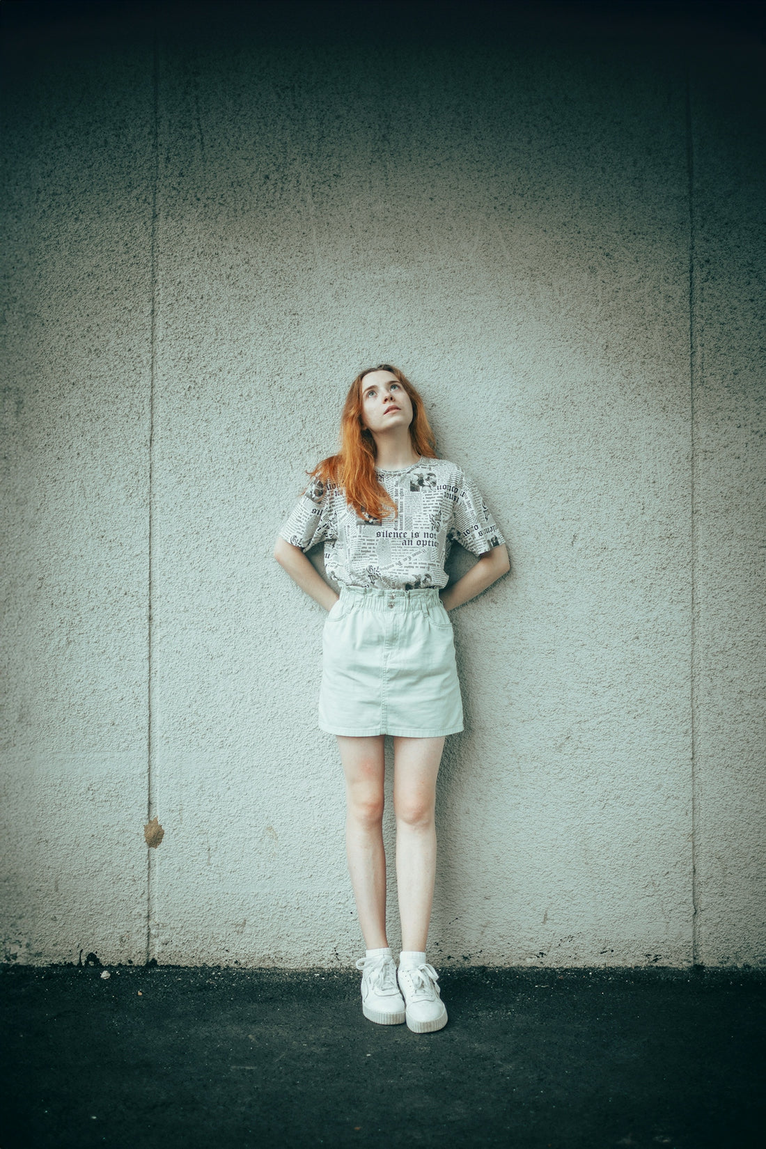 Young woman with red hair looking up against wall