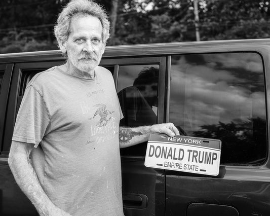Man holding donald trump license plate by car window