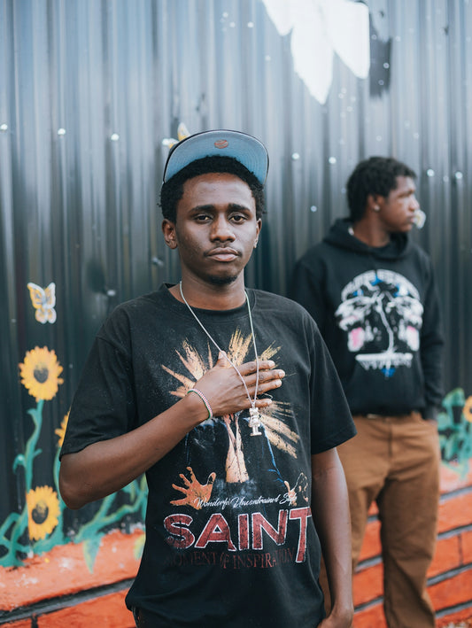 Two young men stand in front of a mural.