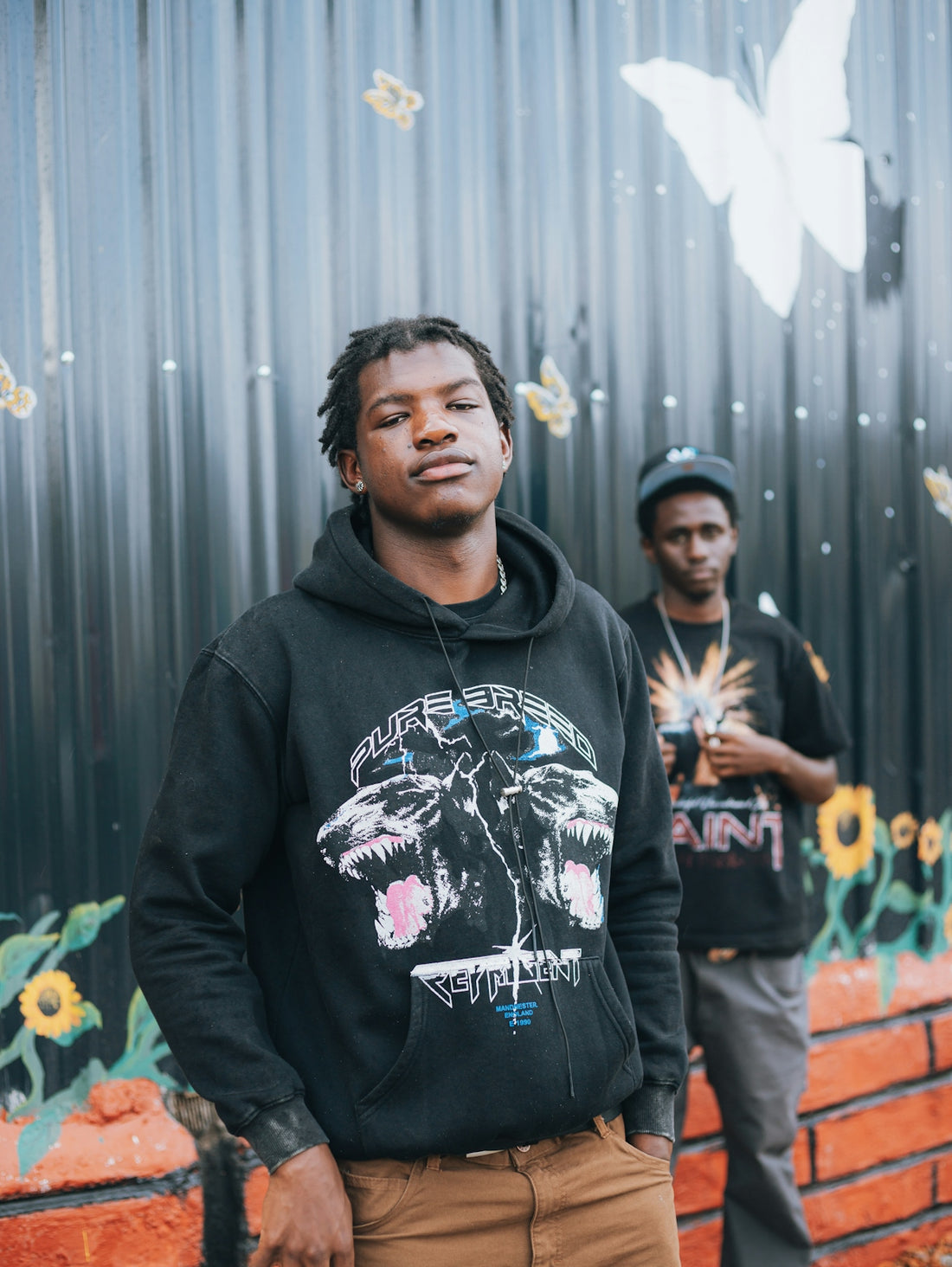Two young men stand in front of a mural