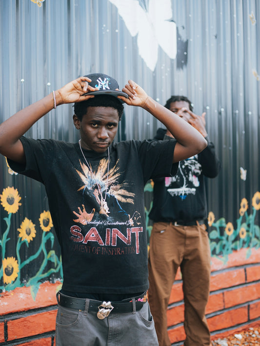 Two young men pose in front of a mural.