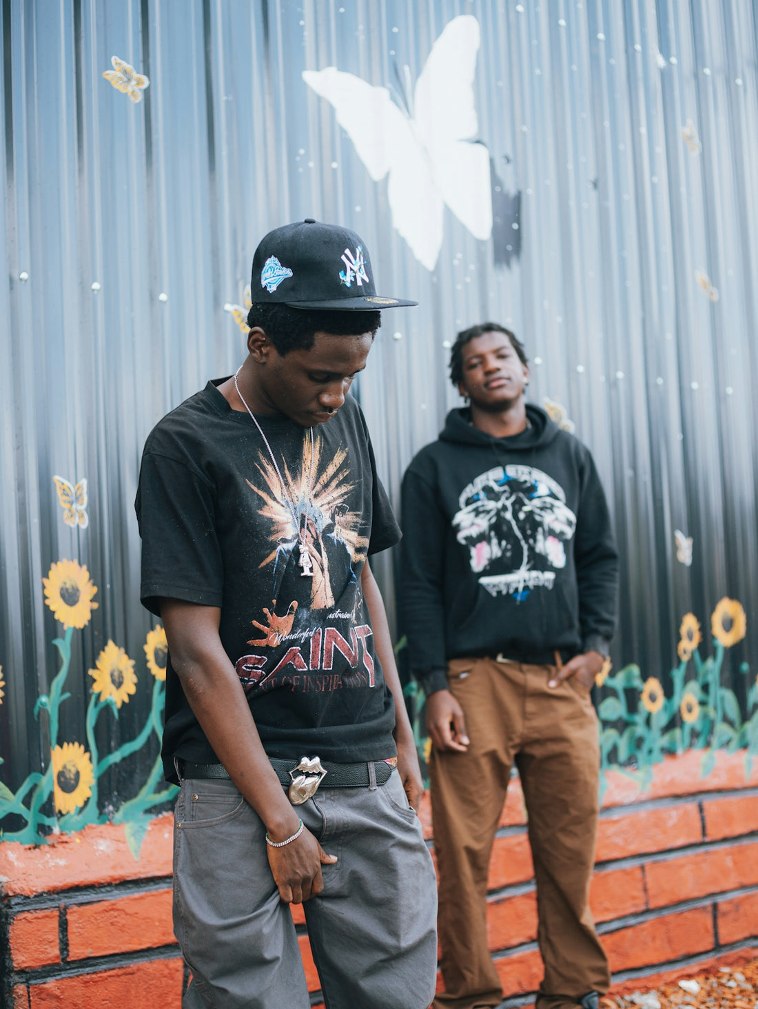 Two young men stand in front of a mural