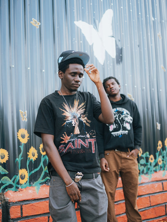 Two young men stand in front of a mural