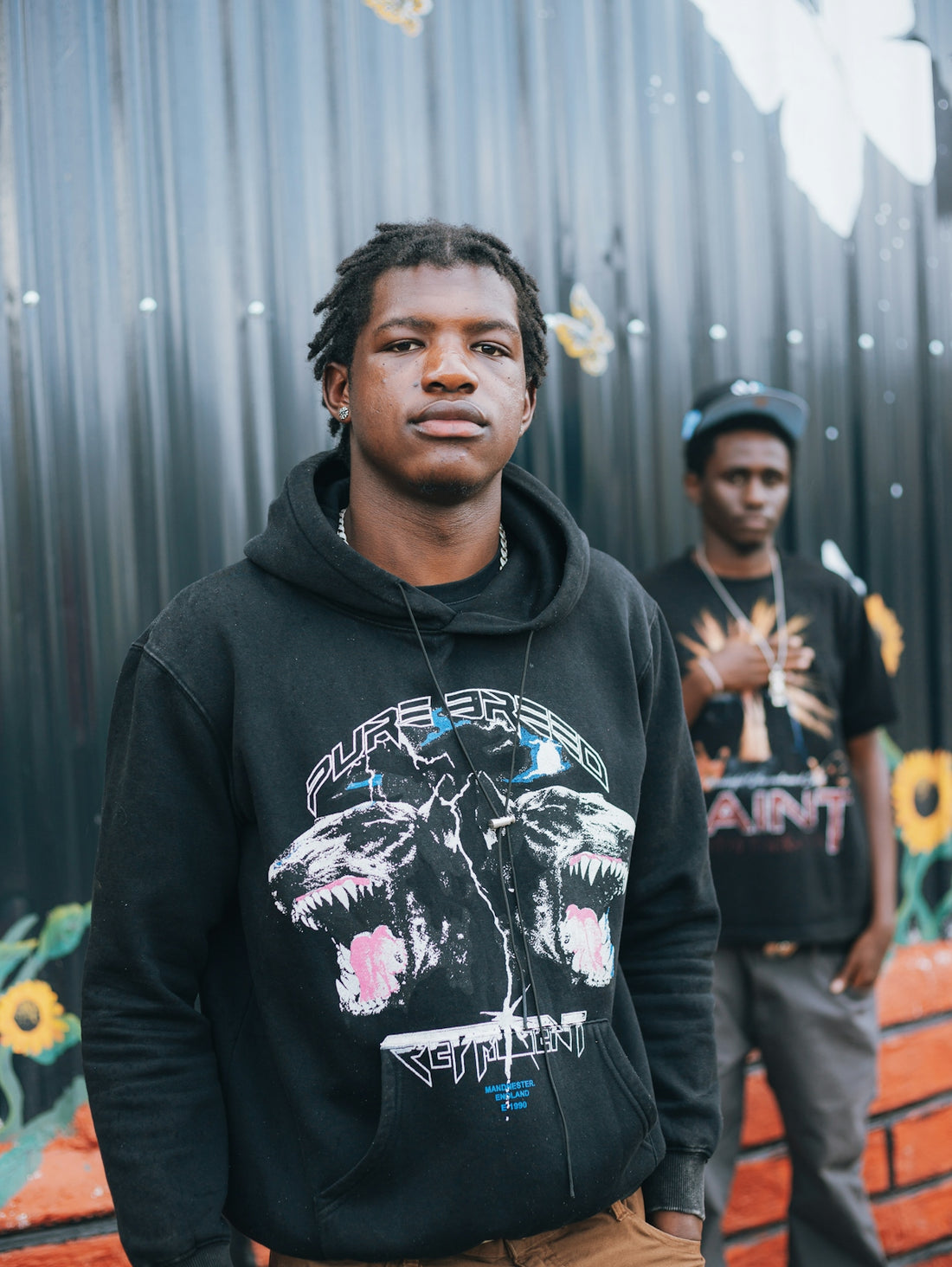Two young men standing in front of a mural