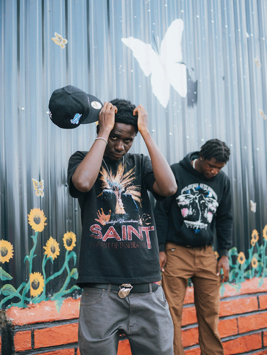 Two young men stand in front of a mural.