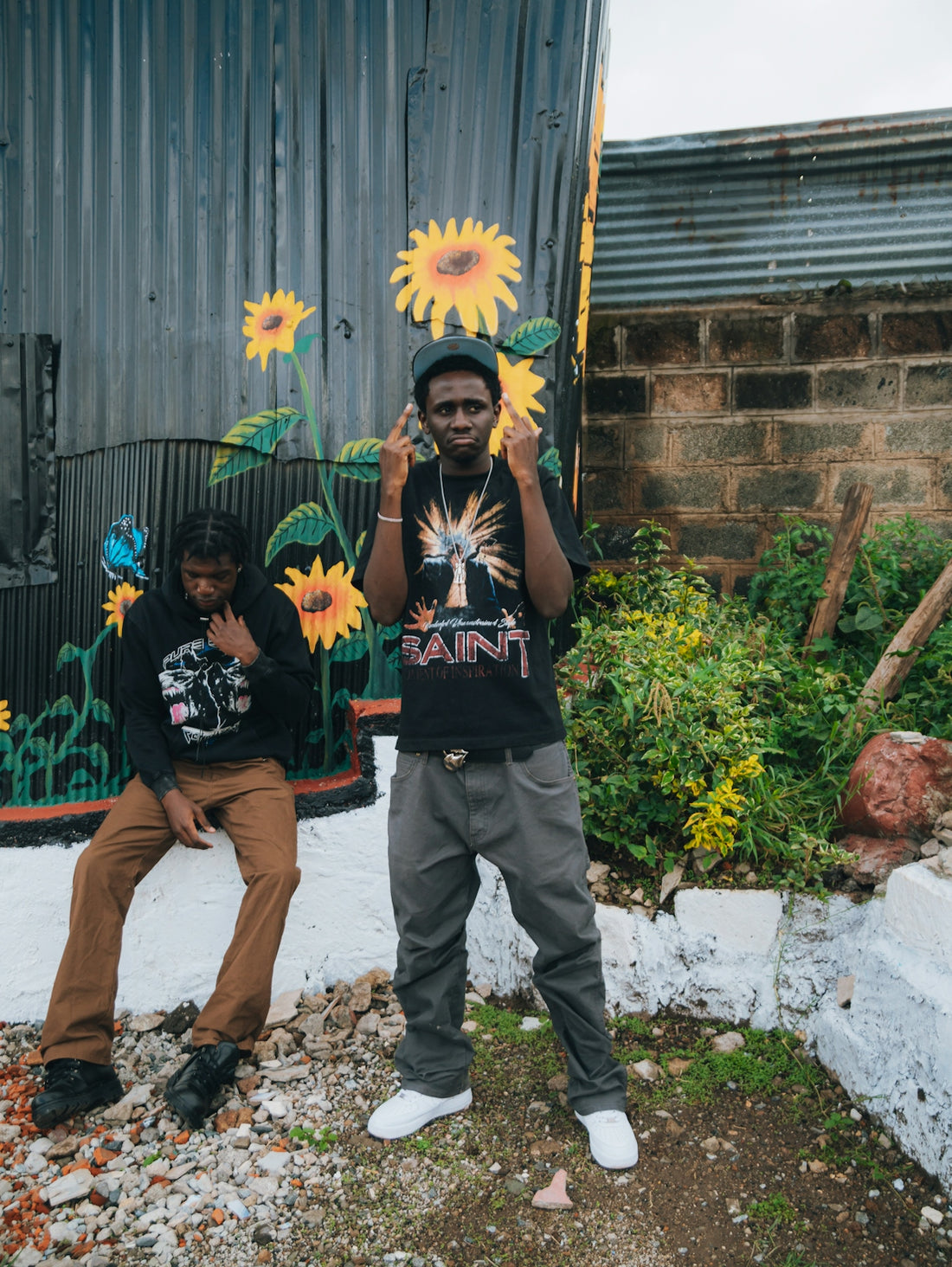 Two young men stand near a mural of sunflowers.