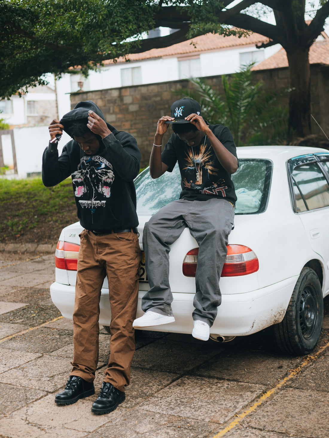 Two young men adjusting hats near a white car