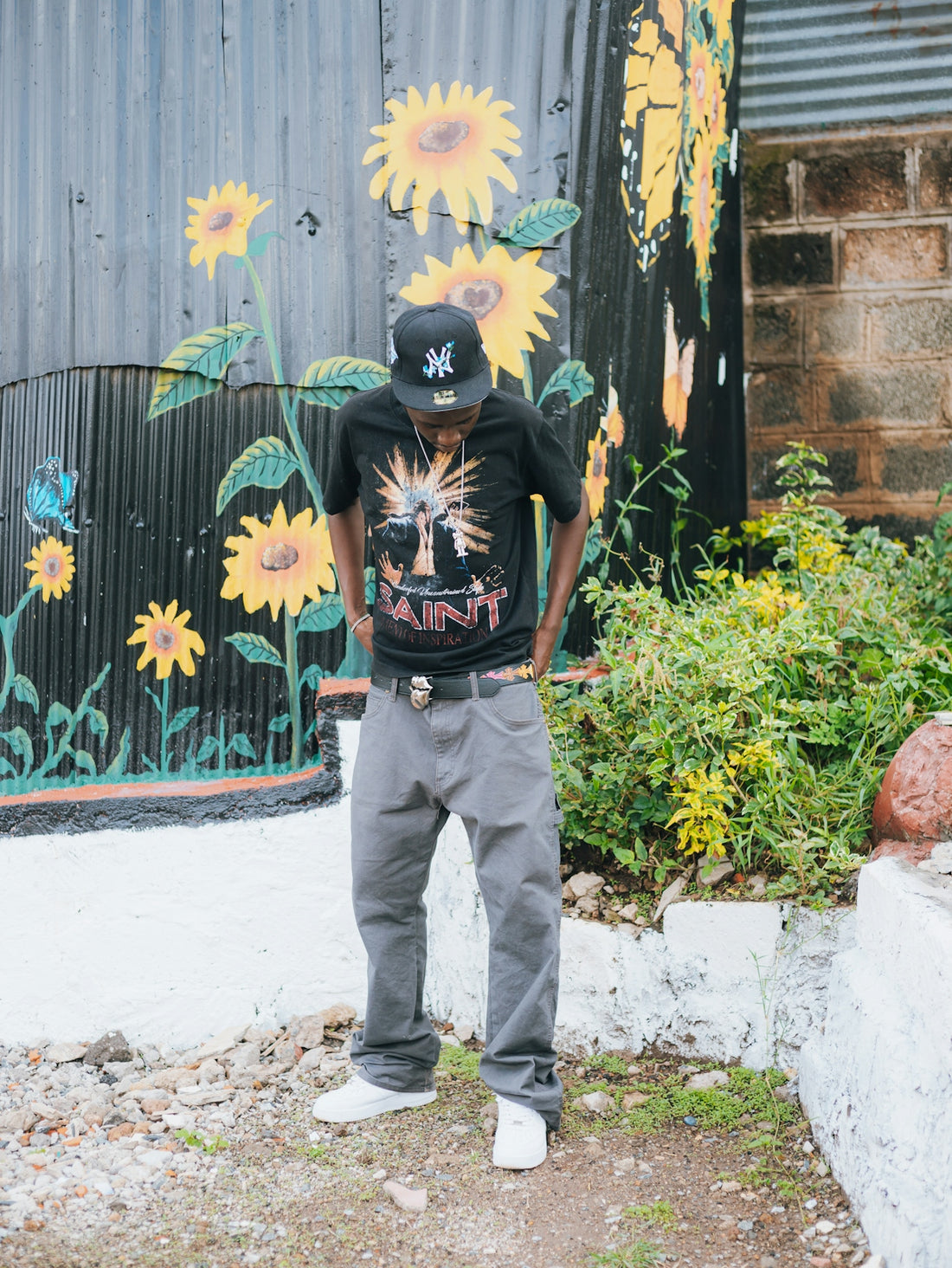 Man in a black t-shirt and grey pants stands outside.
