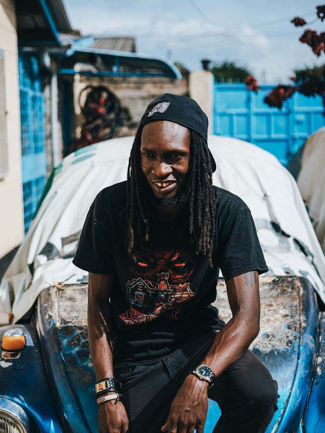 Man with dreadlocks wearing a black t-shirt and cap.