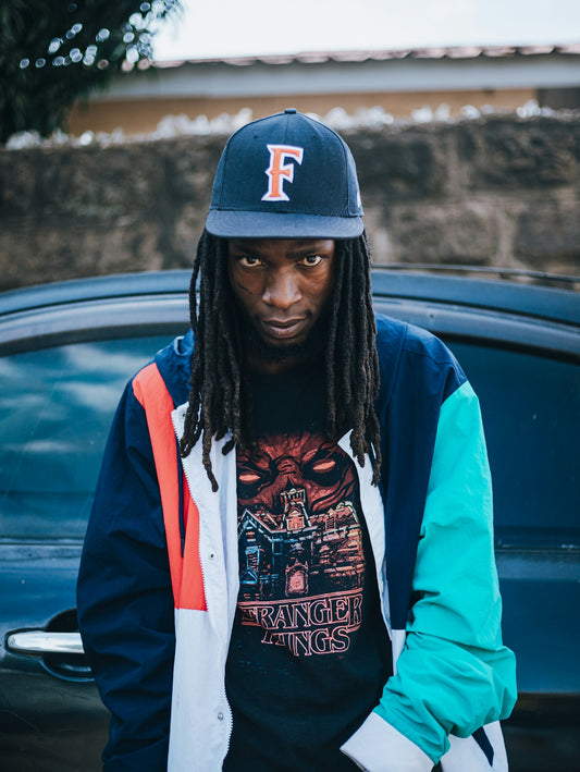 Man with dreadlocks wearing a baseball cap and jacket.