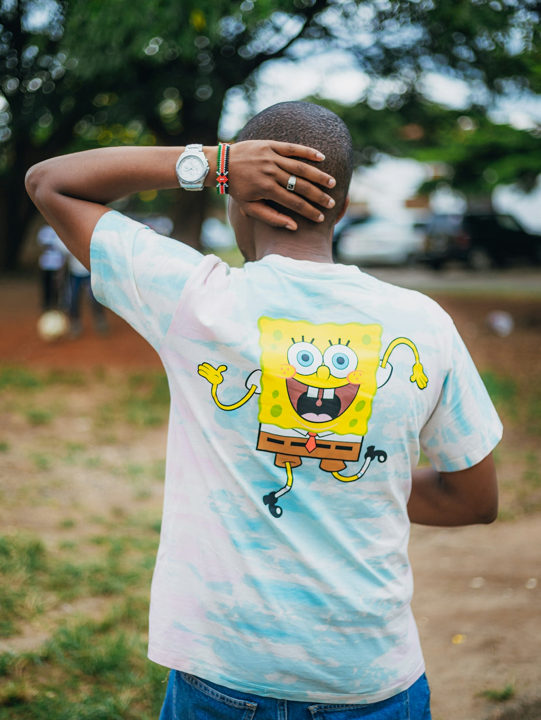 Person wearing spongebob tie-dye shirt outdoors, hand on head.
