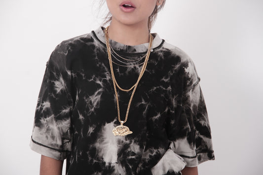 A person wearing a tie-dye shirt and layered gold chains.