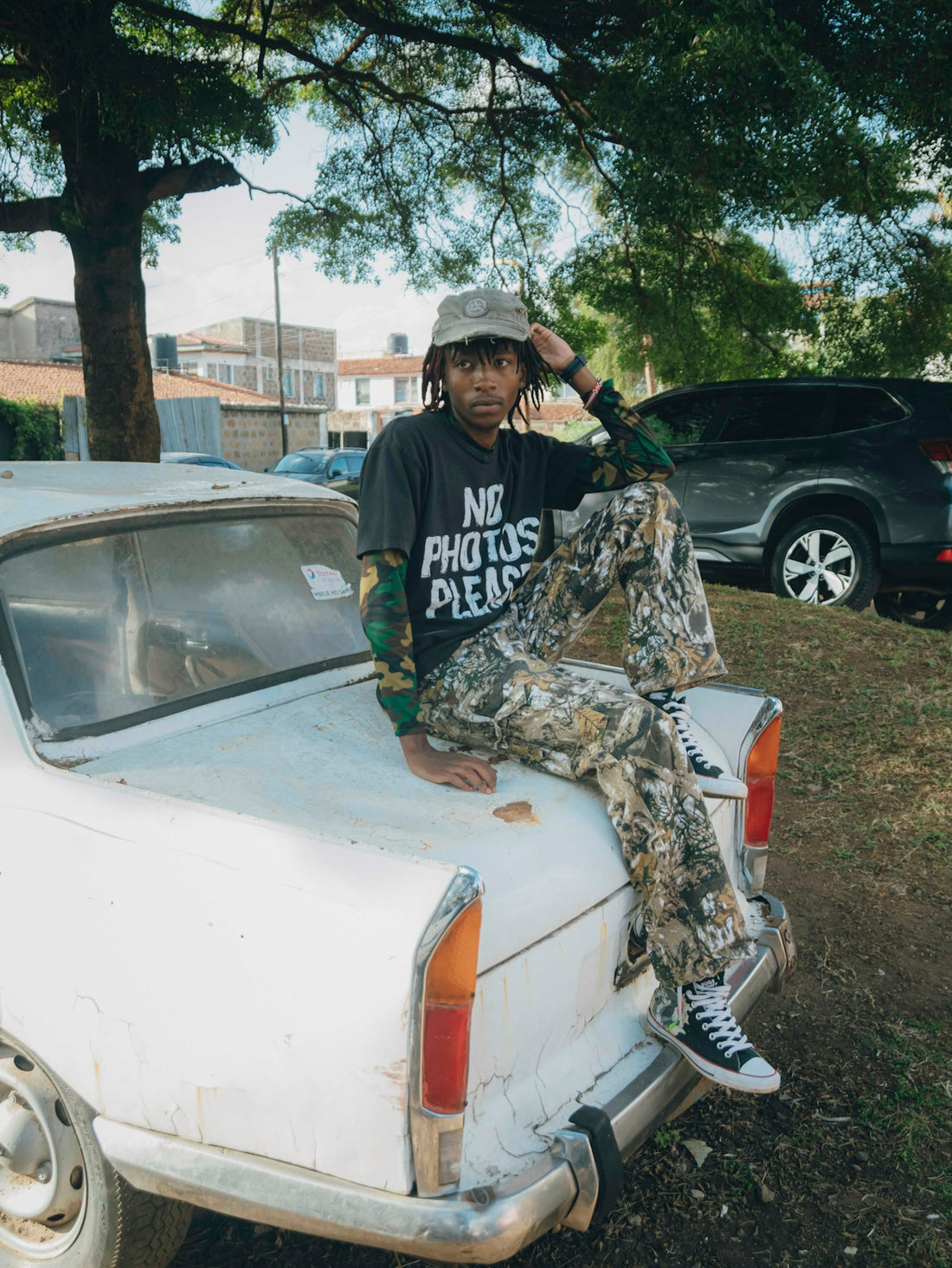 A person with dreadlocks sits on a white car's trunk