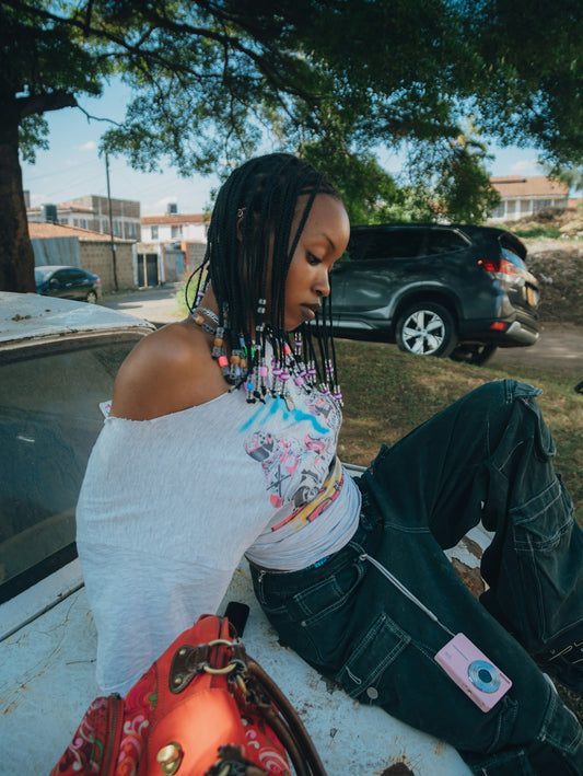 Young woman sits on old car, pink camera on lap