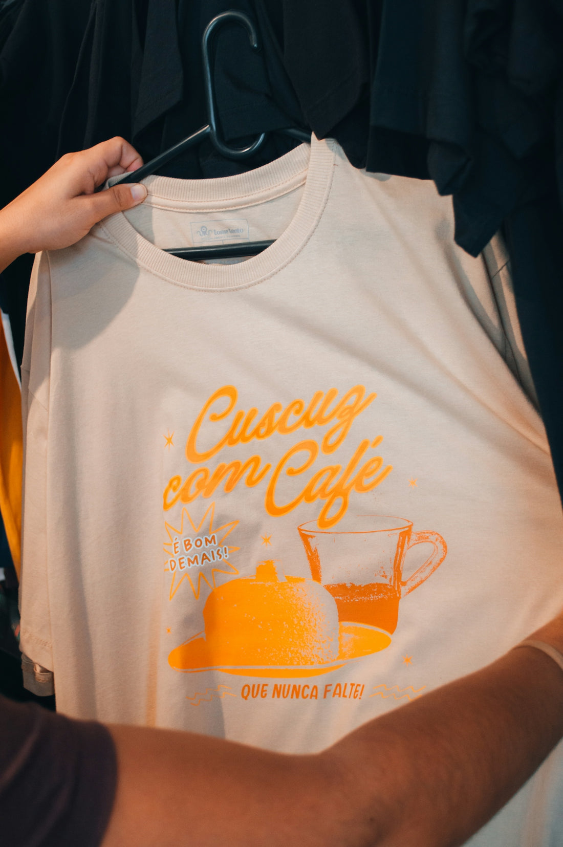 A person holding a beige t-shirt with orange text and a graphic of food